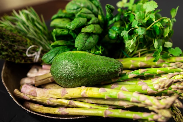 Avocado and various green vegetables on a dark background Asparagus spinach rosemary Vegetarian food concept