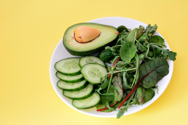 avocado vegetable with cucumber and ruccola on the plate on the yellow background