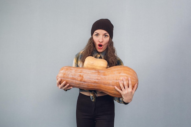 Awesome girl holding big and small pumpkins on a gray background