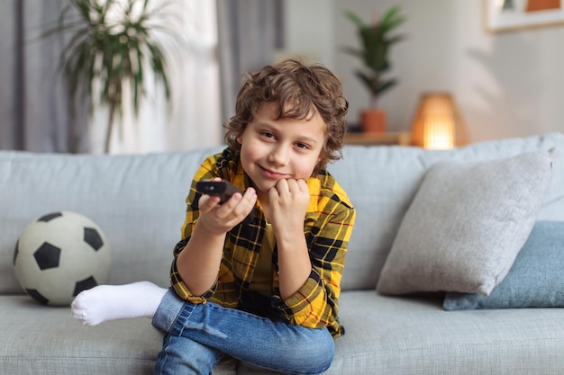 Awesome kids TV Funny little boy choosing videos or movie with remote controller sitting on sofa at home tv set pov