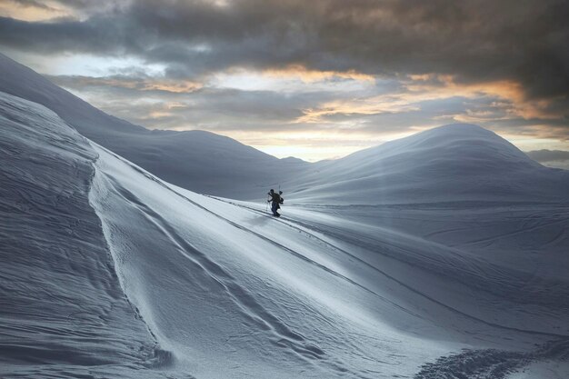 Awesome view of the high snowcapped mountain range and skier walking along it Fog clouds and colorful sky