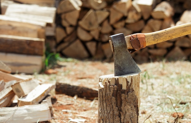 Axe in a stump near the stack of chopped firewood logs. Wood splitting. Close-up.