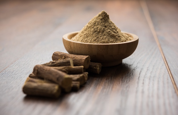 Ayurvedic Mulethi or Liquorice root stick or jeshthamadh powder served in a bowl over moody background