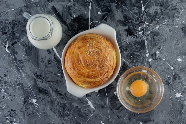 Azerbaijan national pastry with uncooked chicken egg and a glass pitcher of fresh milk . 