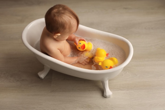 a baby of 11 months is bathing in a white baby bath with rubber ducklings