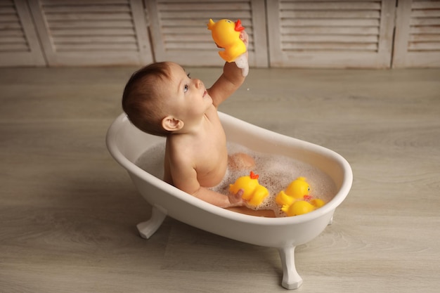 a baby of 11 months is bathing in a white baby bath with rubber ducklings