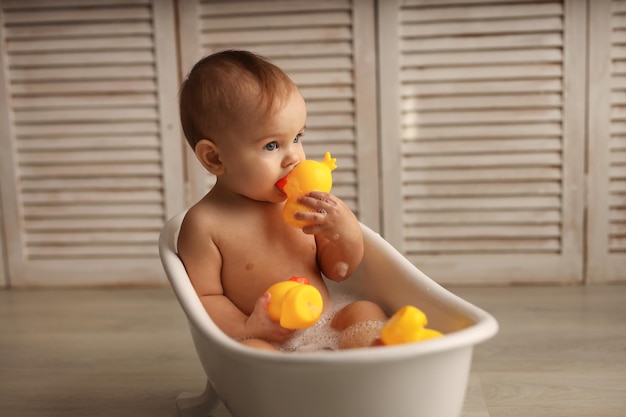 a baby of 11 months is bathing in a white baby bath with rubber ducklings