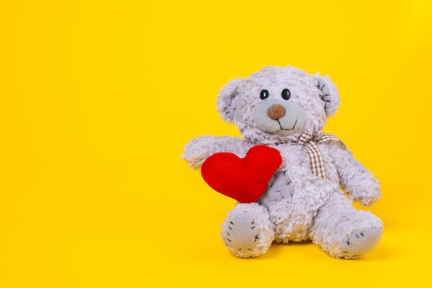 Baby bear toy on a yellow background with copy space gray bear toy with heart on colored background