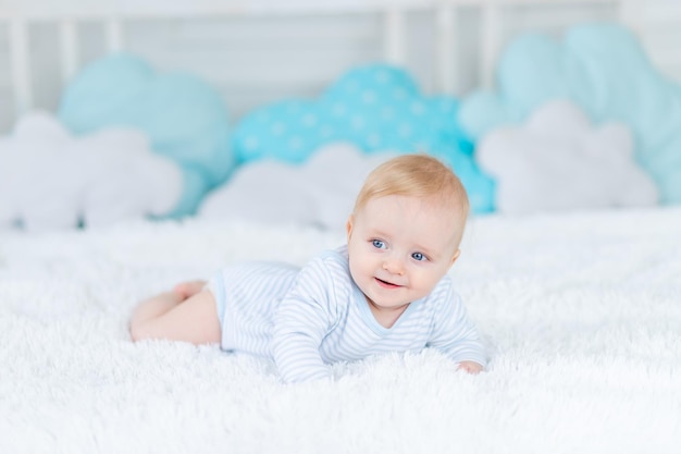 baby on the bed in blue pajamas goes to bed or wakes up in the morning baby boy blonde six months old smiles