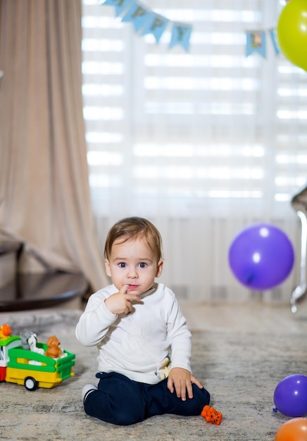 Baby boy celebrates his first birthday around balls and gifts Cute boy playing with colorful balloons