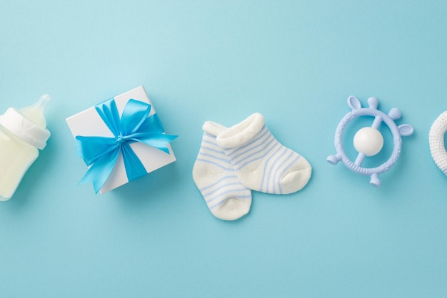 Baby boy concept Top view photo of giftbox teether milk bottle and tiny socks on isolated pastel blue background