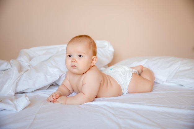 baby boy in a diaper is lying on a white sheet, covered with a blanket in the bedroom on the bed