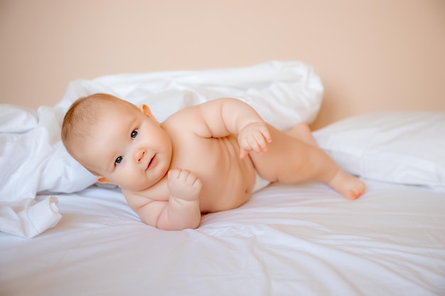 baby boy in a diaper is lying on a white sheet, covered with a blanket in the bedroom on the bed