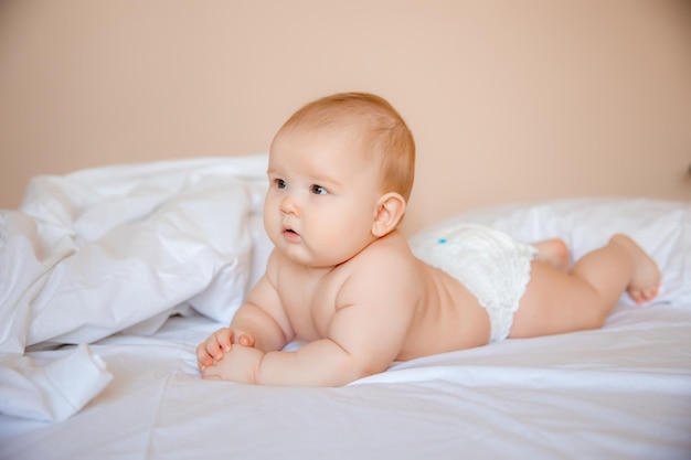 baby boy in a diaper is lying on a white sheet, covered with a blanket in the bedroom on the bed