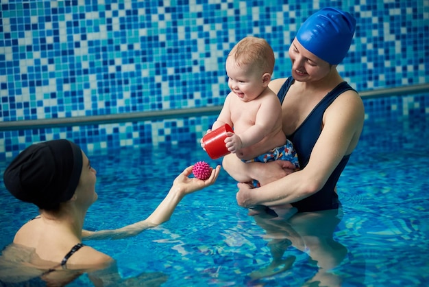 Baby boy and his mother standing in paddling pool Instructor woman playing with baby in pool during swimming classes