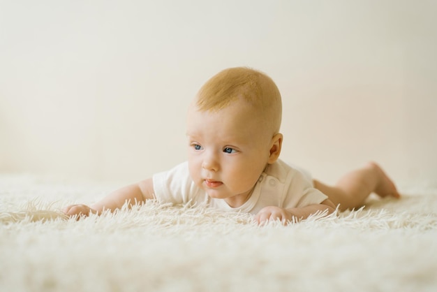 Baby boy is lying on a light blanket on the bed at home