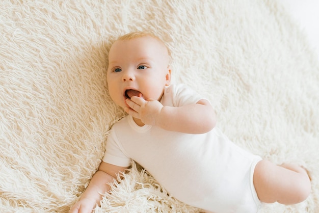 Baby boy lies on a light blanket and holds his hand in his mouth teeth are teething Top view of boy