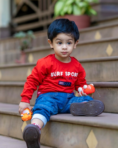 baby boy playing with toys sitting in stairs wearing red t shirt and blue jeans