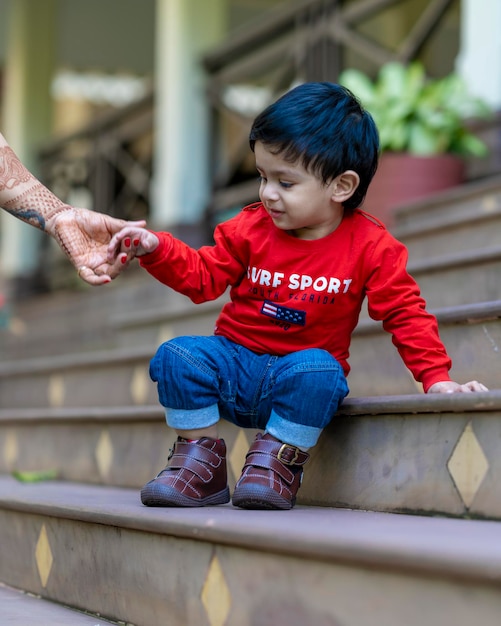 baby boy playing with toys sitting in stairs wearing red t shirt and blue jeans