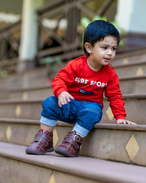 baby boy playing with toys sitting in stairs wearing red t shirt and blue jeans