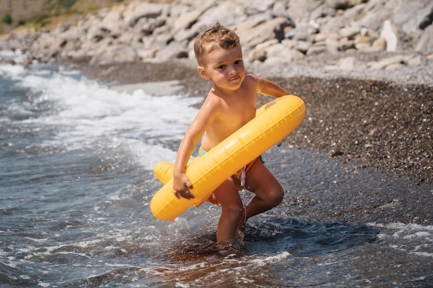 Baby boy runs into the sea in a yellow inflatable circle The child is preparing for swimming He is happy and laughing