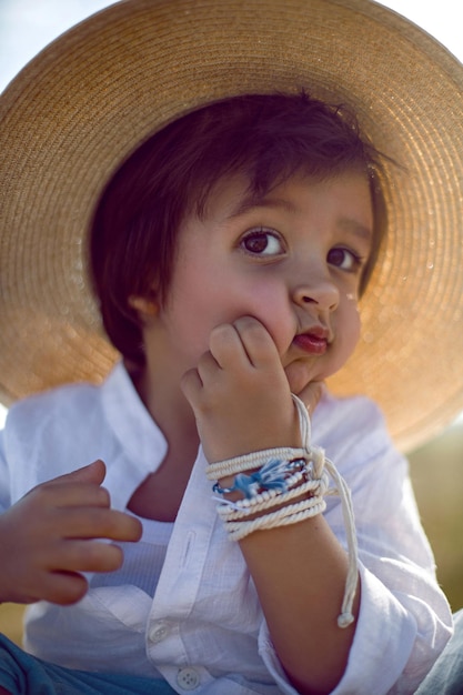 Baby boy in straw hat and blue pants sitting on a haystack in a field in autumn