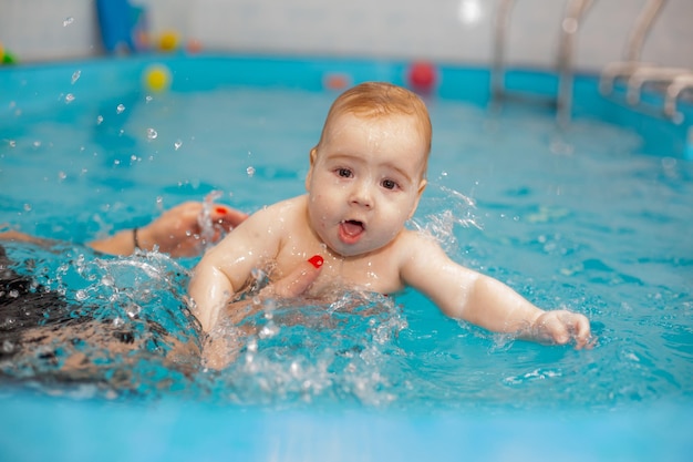 Baby boy trains to swim in the pool with a trainer