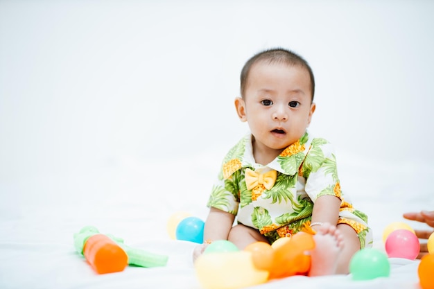 Baby boy wearing a colorful suit is happy and smiles with toys in white room