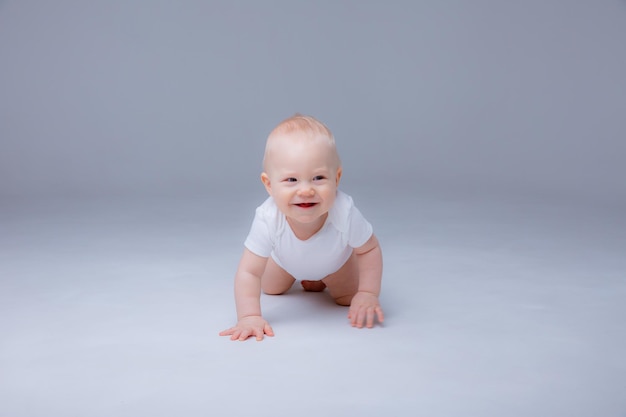 Baby boy in a white bodysuit crawling on a white background