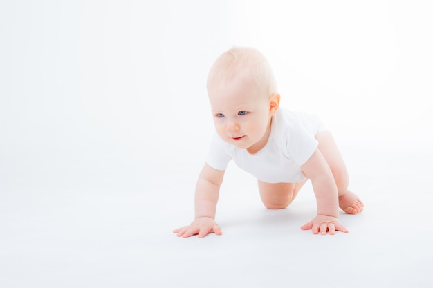 Baby boy in a white bodysuit crawling on a white background