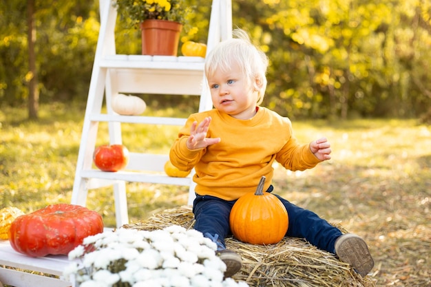 Baby boy with pumpkin in his hands in autumn park background with golden trees