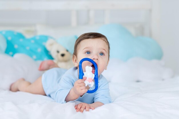 Baby boy with a rodent for teething or a rattle on the bed for sleeping, healthy happy little baby in a blue bodysuit playing