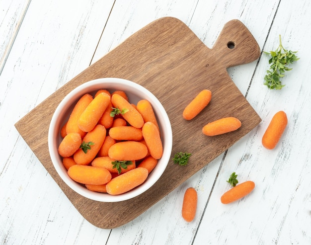 Baby carrots in a bowl over wooden table with herbs