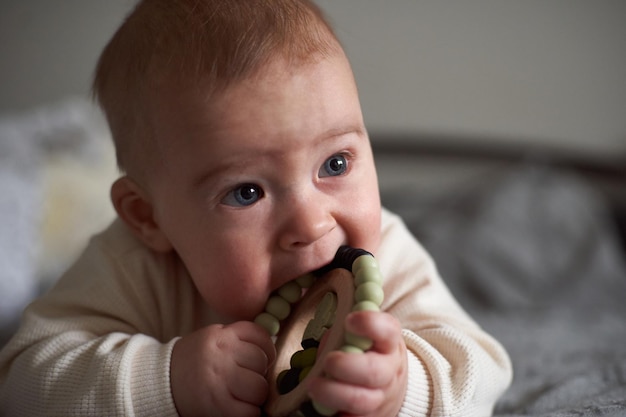 Baby chewing teether toy Infant growing first tooth Boy biting toy on parents bed Pretty sixmonth old baby boy Realistic toddler home portrait