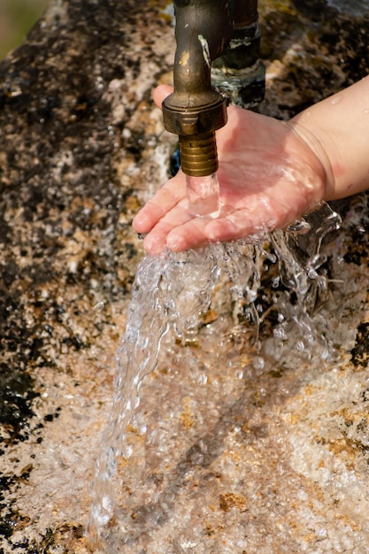 Baby cleaning his hands at an outdoor tap coming out of a stone refreshing splashes without wasting water