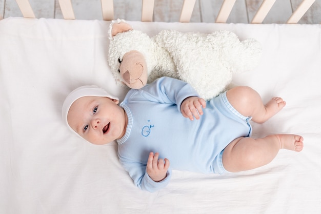 Baby in the crib, laughing baby 3 months lying with a teddy bear toy, children and birth concept