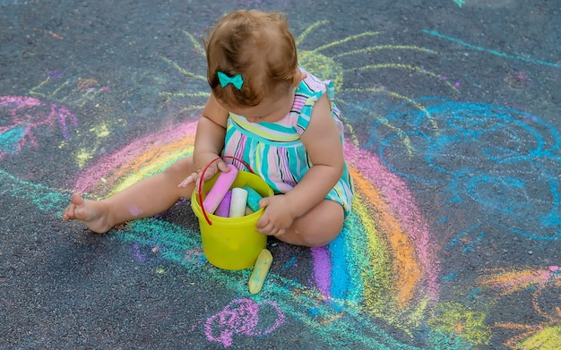 Baby draws a rainbow on the pavement with chalk. Selective focus. Nature.