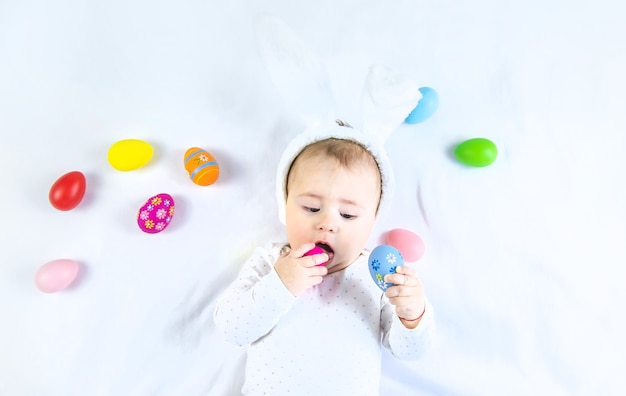 Baby dressed like a bunny with Easter eggs for Easter holiday on white surface