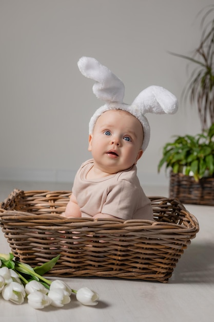 baby in an Easter bunny costume is sitting in a wicker basket on the floor with tulips