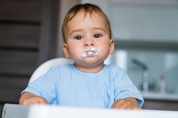 Baby eating food on kitchen Feeding baby food to baby Grimy funny child eats porridge in the chair