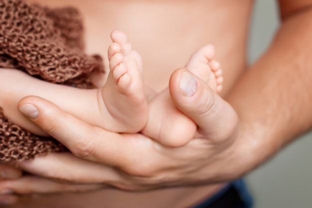 Baby feet in father hands. Tiny Newborn Baby's feet on male shaped hands closeup. Dad and his Child. Happy Family concept.