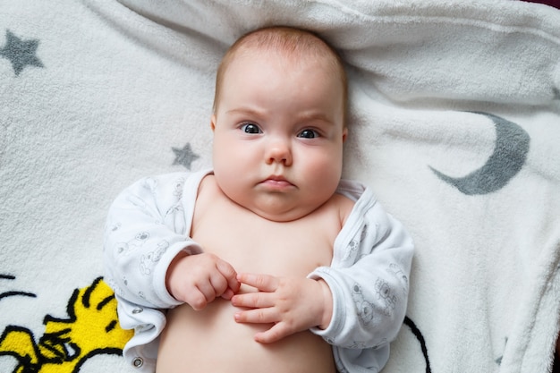 Baby girl 3 months old is lying on the bed. Baby without clothes in a diaper