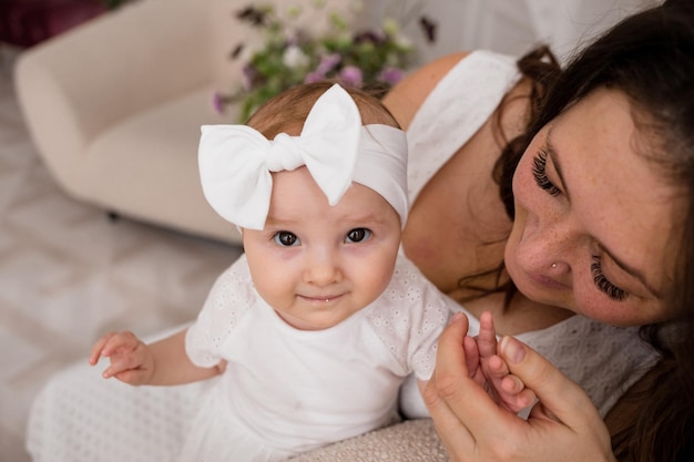 A baby girl in a bandage is sitting on the sofa in the arms of her mother