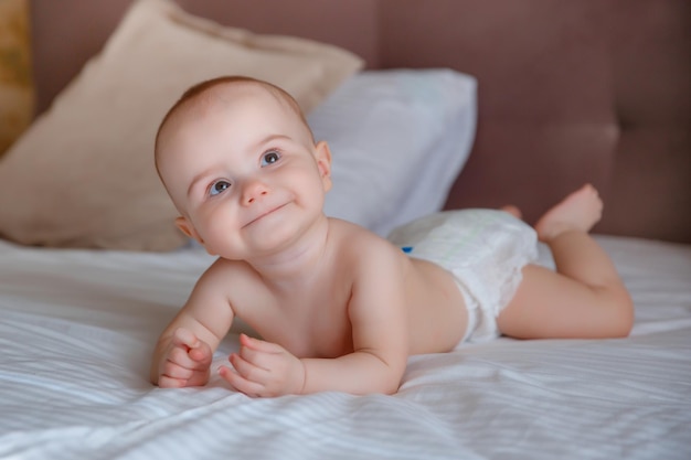 baby girl in a diaper is lying on the bed in the bedroom on his stomach smiling