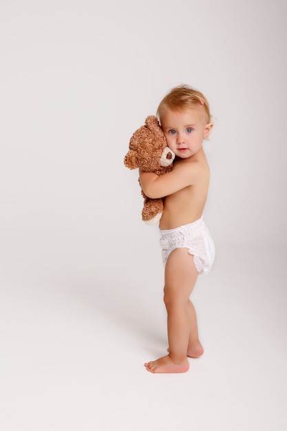 Baby girl in diaper playing with Teddy bear on white 