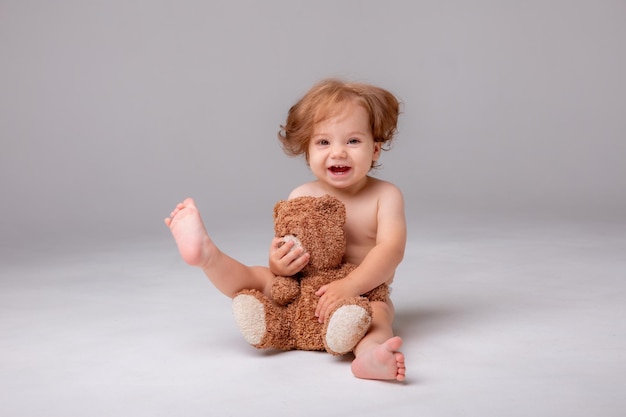 A baby girl in a diaper sits and plays hugs with a teddy bear on a white background