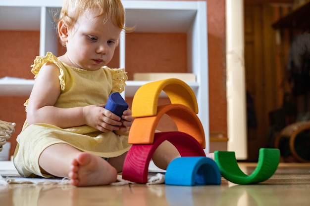 Photo baby girl in dress stacking rainbow arch block construction building ecological wooden toy tower