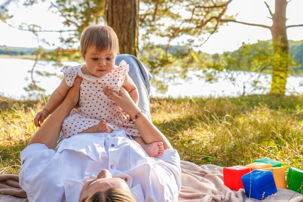 baby girl in her mother's arms plays in the park in summer