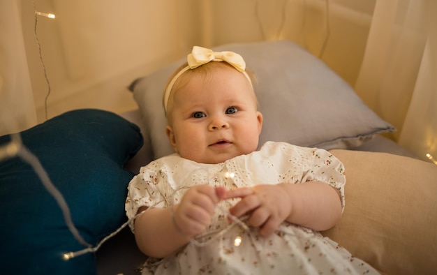 Baby girl is lying in bed on a mattress under a canopy and playing with a garland