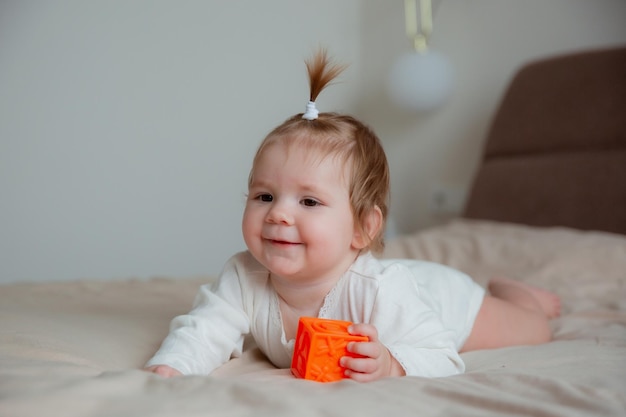 The baby girl is sitting at home on the bed in the bedroom playing with cubes